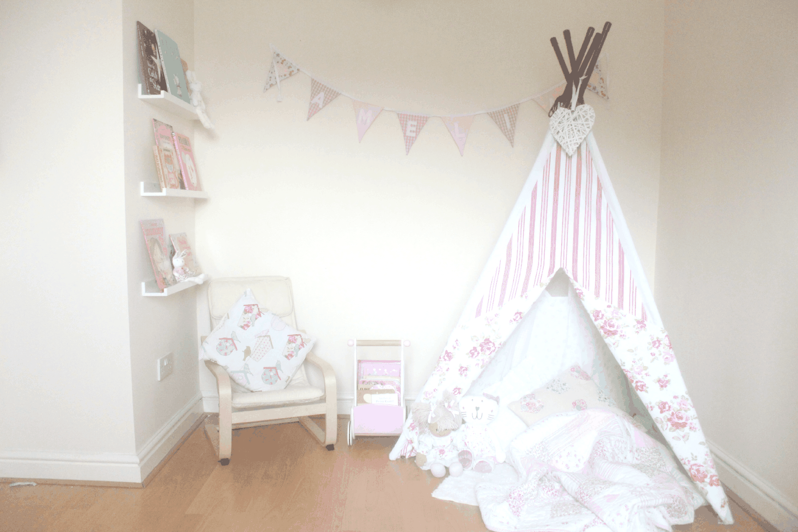 A cozy corner with a pink and white striped teepee tent, cream armchair, and bunting banner, evoking the warmth of family life at home.